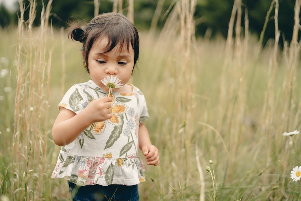 little girl in field smelling a flower