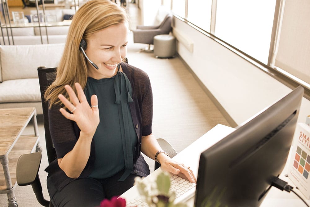 women at computer wearing a headset waving